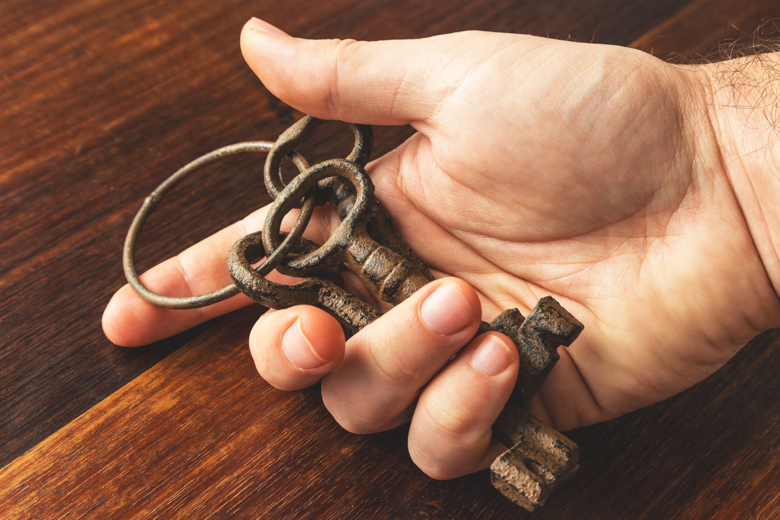 high-angle-shot-person-holding-some-old-rusted-keys-wooden-surface (1)
